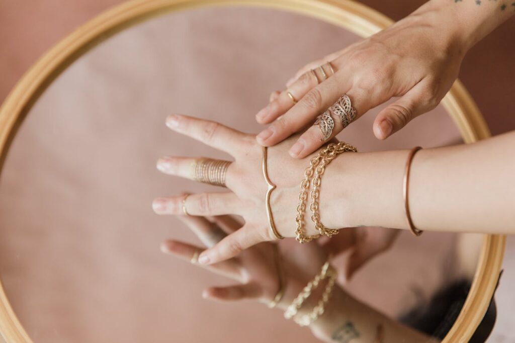 Close-up of elegant hands with jewelry, reflecting on a mirror surface.